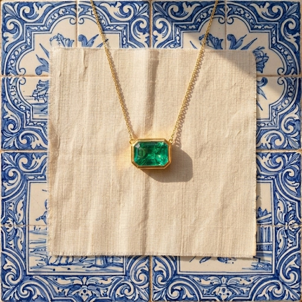18K gold necklace with a emerald pendant on a beige fabric against a blue and white tiled background